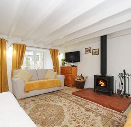 A living room with sofas yellow curtains a television and a wood burning stove at Henwood Barn in Henwood near Upton Cross