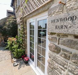 Exterior view of stone building with glass double doors plants and a sign reading Henwood Barn Henwood near Upton Cross