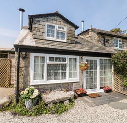 Stone cottage exterior with white window frames flower pots and a gravel pathway at Mole Cottage Henwood near Upton Cross