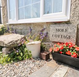 A stone wall with a window and a sign that says Mole Cottage with flowers and a stone slab at Mole Cottage in Henwood near Upton Cross