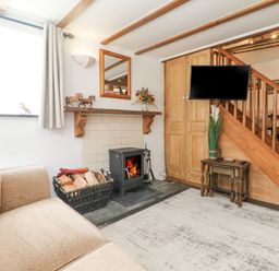 A living room with a sofa a small wood burning stove and firewood under a window and a television on the wall at Mole Cottage in Henwood near Upton Cross