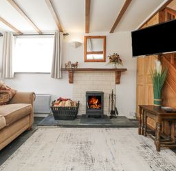 A living room with a sofa a fireplace with firewood a wall-mounted television and a wooden staircase at Mole Cottage in Henwood near Upton Cross