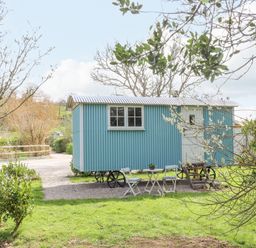 A blue shepherds hut on wheels with a small table and chairs outside in a grassy garden at Gwithian Shepherds Hut Angarrack near Hayle