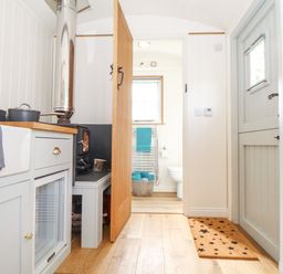 A small kitchen area with a stove sink and pots next to a wooden door leading to a bathroom with a towel rack and toilet at Gwithian Shepherds Hut Angarrack near Hayle