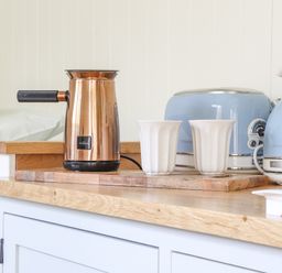 A wooden countertop with a copper milk frother two white cups a blue toaster and a blue kettle at Gwithian Shepherds Hut in Angarrack near Hayle