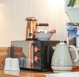 A kitchen counter with a microwave, electric kettle, coffee pot, mugs, and informational books at Godrevy Shepherds Hut in Angarrack near Hayle