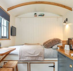A small room with a bed table stools and kitchen appliances at Godrevy Shepherds Hut in Angarrack near Hayle