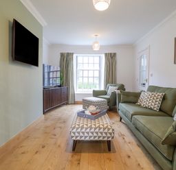 A living room with green sofa and armchair wooden floor and wall mounted tv at 23 Church Farm Lane in Halesworth