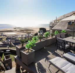 A terrace with outdoor seating and plants overlooking a beach and town at Ty'n-Y-Ffynnon Cottage in Barmouth