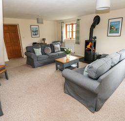 A living room with two grey sofas a wood burning stove and a wooden coffee table at Ty Rhosyn in Penycwm near Solva