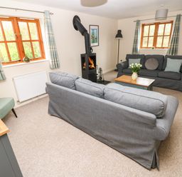 A living room with two gray sofas a wood stove and two windows with plaid curtains at Ty Rhosyn in Penycwm near Solva