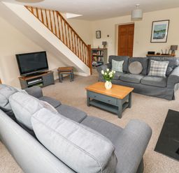 A living room with two grey sofas a wooden coffee table with flowers a television under stairs and a stove at Ty Rhosyn in Penycwm near Solva