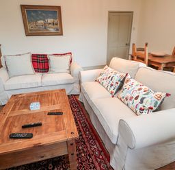 A living room with two white sofas, a wooden coffee table, a dining table with chairs, and framed pictures on the wall at Upper Oakwood in Alnwick