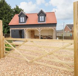 A gravel driveway with a wooden gate leading to a black house with a red roof and two dormer windows at Strawberry Fields Annex in Emneth