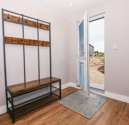 An entryway with a wooden bench coat rack a grey floor mat an open door leading outside and a fire extinguisher mounted on the wall at Strawberry Fields Annex in Emneth