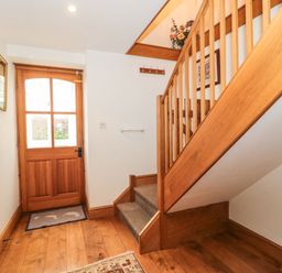 A hallway with wooden stairs a wooden door and a mirror on the wall at Oak Barn in Kentisbeare