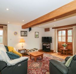 A living room with leather sofas, a wooden coffee table, a television, and wooden doors at Oak Barn in Kentisbeare