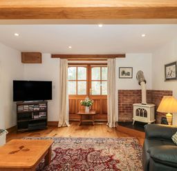 A living room with a television and a stove next to a window with curtains at Oak Barn in Kentisbeare