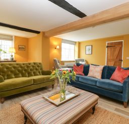 A living room with green and blue sofas a striped ottoman a wooden door and windows at Byways Madresfield near Malvern