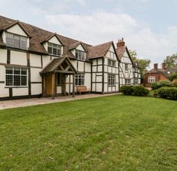 A large white and black timber framed house with a pitched roof and green lawn in front at Byways in Madresfield near Malvern