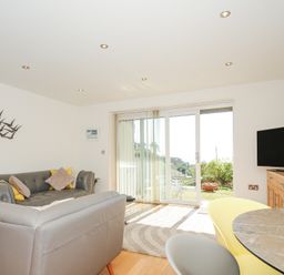 A living room with leather sofas sliding glass doors and a television at Pebbles in Downderry