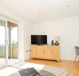 A living room with wooden cabinet and TV near glass sliding door at Pebbles in Downderry