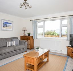 A living room with a grey sofa wooden coffee table wooden cabinet and television at 7 Maes Awel in Abersoch