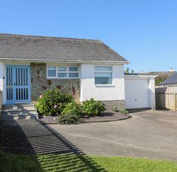 A white house with a blue door driveway garden bushes and an attached garage at 7 Maes Awel in Abersoch