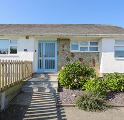 Front exterior of a single-story house with a light blue door and surrounding garden at 7 Maes Awel in Abersoch