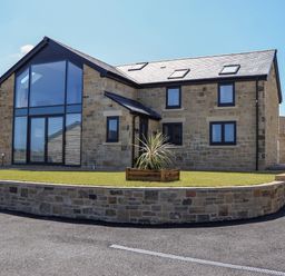 A stone house with large glass windows and a small lawn with a plant at The Waves in Amble