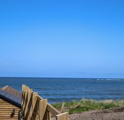 A wooden fence and a small wooden building near the sea with grassy land at The Waves in Amble