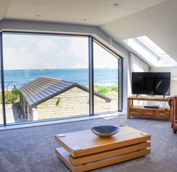 A living room with a large window overlooking the sea a wooden coffee table a television on a wooden stand and a leather sofa at The Waves in Amble