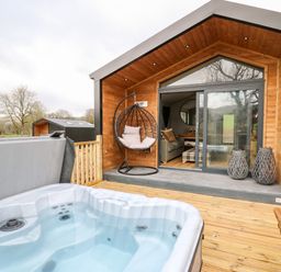 An outdoor deck with a hot tub a hanging chair and a wooden cabin with sliding glass doors at Fawn's Rest in Nantmel near Rhayader