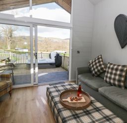 A living room with a sofa and armchair leading to a deck at Doe Lodge in Nantmel near Rhayader