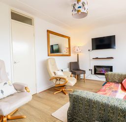 A living room with an armchair a sofa a wall mirror a television and a floor lamp at Sandpiper in Perranporth