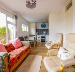 A living room with a sofa and armchairs next to a dining table and kitchen at Sandpiper in Perranporth