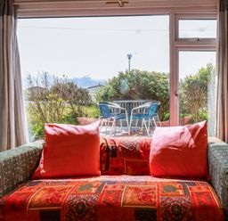 A sofa with cushions in front of a large window overlooking a patio with table and chairs at Sandpiper in Perranporth
