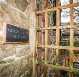 Stone wall with Church How Cottage sign wooden lattice gate outside a stone building with picnic table and leaf-covered ground at Church How Cottage in Nether Wasdale