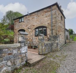 A stone building with arched windows and a stone wall gate at The Coach House in Trelogan Hall Trelogan near Trelawnyd