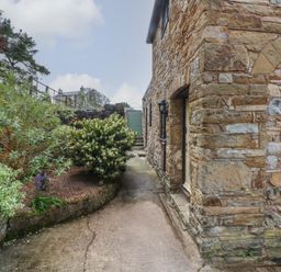 A stone building next to a paved pathway with plants and shrubs alongside at The Coach House in Trelogan Hall Trelogan near Trelawnyd