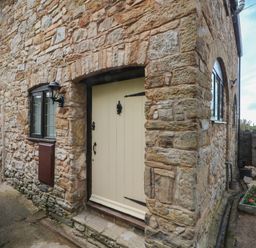 A stone exterior wall with a cream door and windows next to a flower bed and a wish well at The Coach House Trelogan Hall Trelogan near Trelawnyd