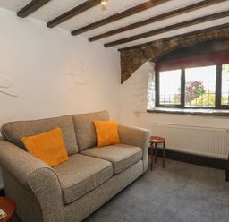 A living room with a sofa two orange cushions side tables and a window at The Coach House Trelogan Hall Trelogan near Trelawnyd