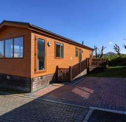 An exterior view of a wooden cabin with windows a door and a ramp on a paved area at Daffodil Lodge in Mullacott near Ilfracombe