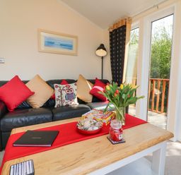 A living room with a black leather sofa with cushions and a wooden coffee table with flowers and games at Poppy Lodge in Mullacott Ilfracombe
