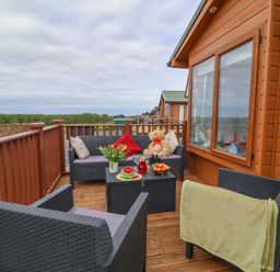A wooden balcony with outdoor furniture a teddy bear and a small table with fruit at Poppy Lodge in Mullacott Ilfracombe