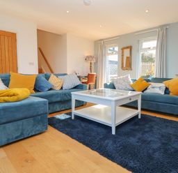 A living room with blue sofas yellow cushions white coffee table and wooden doors at Chilowan in Trewarmett near Tintagel