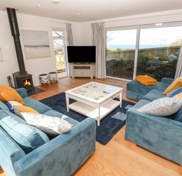 A living room with blue sofas a white coffee table and a wood burning stove at Chilowan in Trewarmett near Tintagel