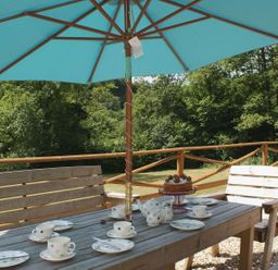 An outdoor wooden table set with cups plates teapot and cake under a blue umbrella surrounded by wooden chairs on a deck at Valley Lodge Oakfordbridge near Bampton