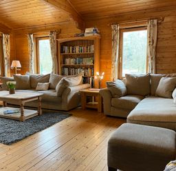 A living room with two sofas a wooden coffee table a bookshelf and windows at Valley Lodge Oakfordbridge near Bampton
