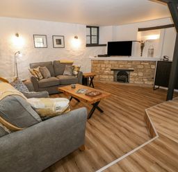 A living room with two grey sofas wooden coffee tables a small fireplace and a television at Ellie's Cottage in Burford